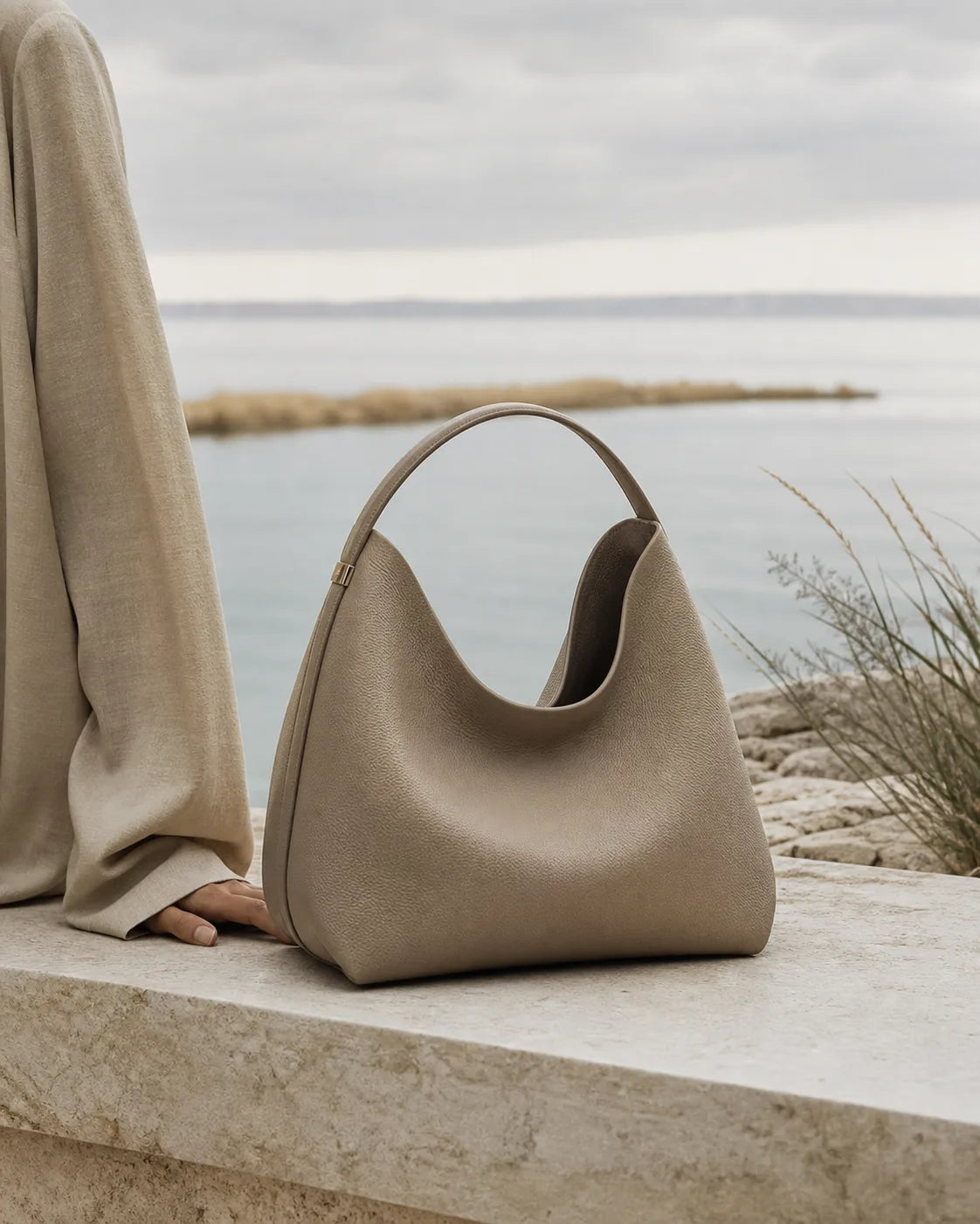 Taupe AELA handbag on limestone beside muted water